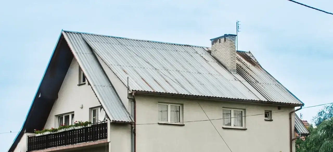 Szary dach z blachy falistej, z widocznym kominem. Zastanawiasz się nad malowanie dachu cena?