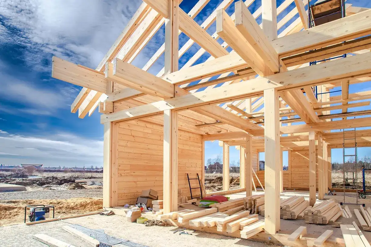 La charpente d'une maison en bois prend forme sous un ciel bleu. Des poutres de bois sont assemblées pour construire une nouvelle demeure.