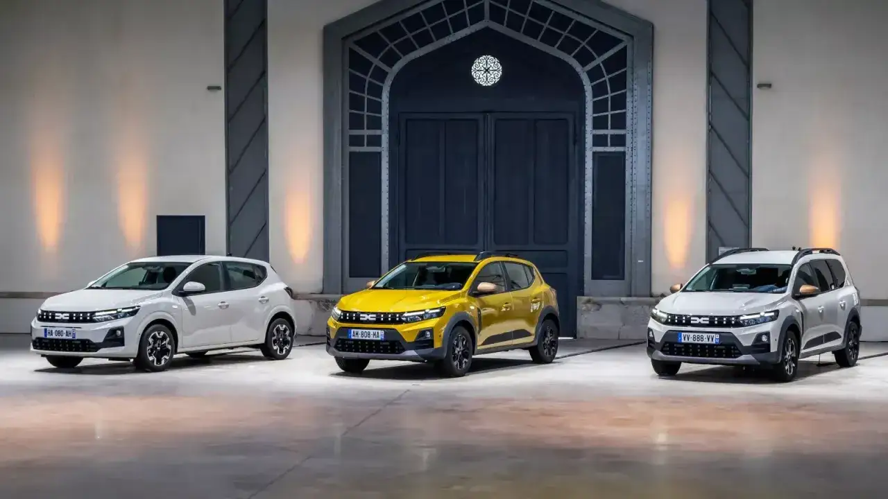 Trois Dacia Sandman, une jaune et deux blanches, align&eacute;es devant une grande porte.