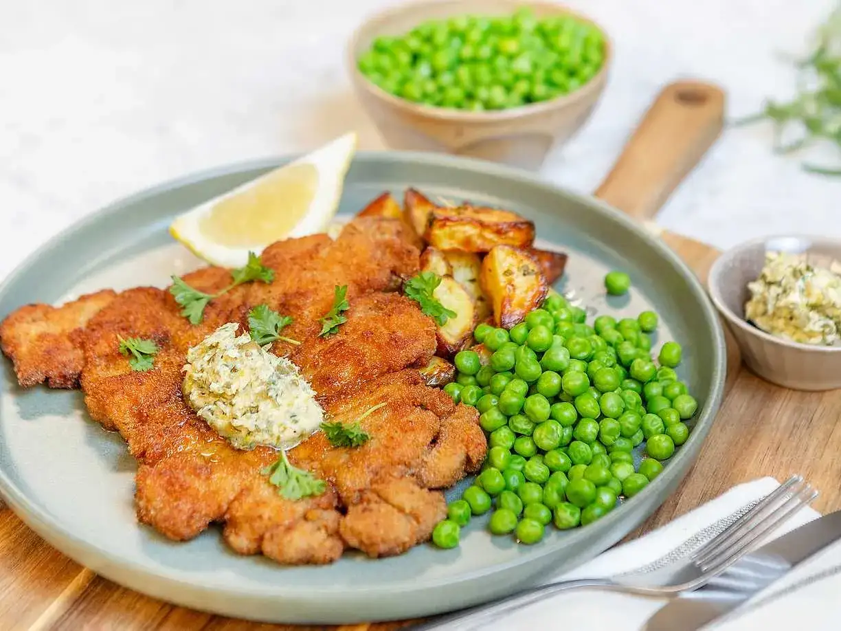 En gyllene schnitzel med örtsmör, rostade potatisar och gröna ärtor. Ett perfekt schnitzel recept för en härlig middag.