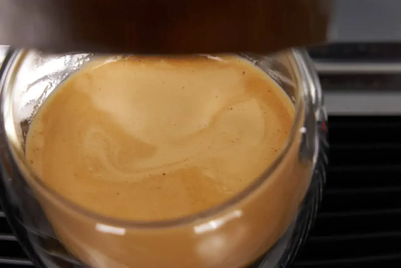 Ein Glas mit cremigem Kaffee, das ist cafe crema mit milch. Die goldbraune Crema bildet sanfte Wellen.