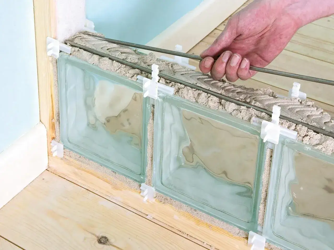 Pose de brique de verre extérieur : un ouvrier insère des barres de fer dans le mortier pour renforcer la structure.