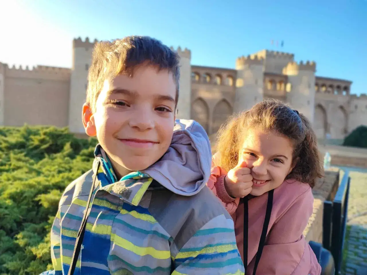 Dos niños sonríen frente a un castillo, disfrutando de actividades gratis para niños en Zaragoza.
