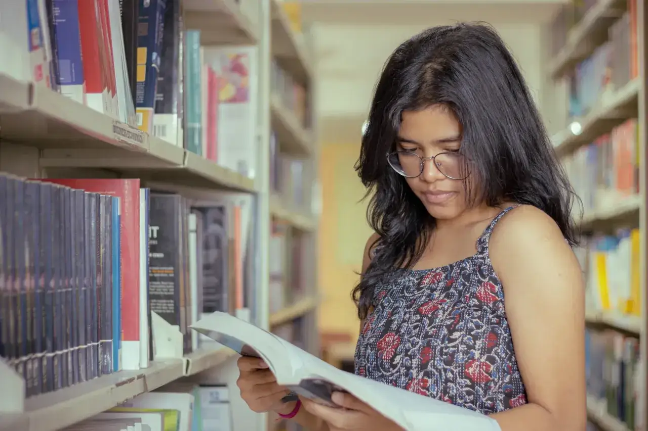 Une jeune femme choisit un livre dans une biblioth&egrave;que, peut-&ecirc;tre &agrave; la recherche du top 10 des livres pour adolescent.
