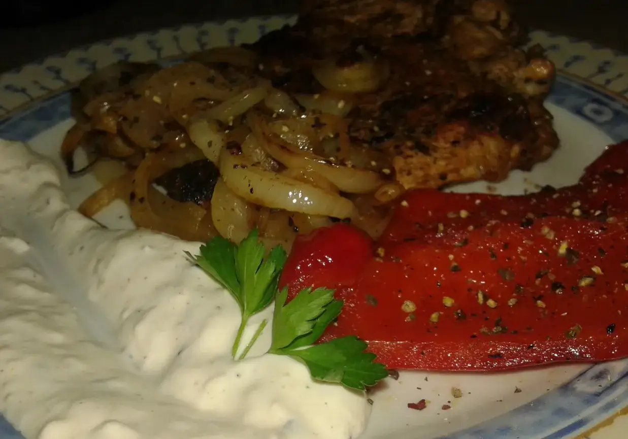 Pyszny stek wieprzowy z duszonymi cebulkami, pieczoną papryką i kremowym sosem.