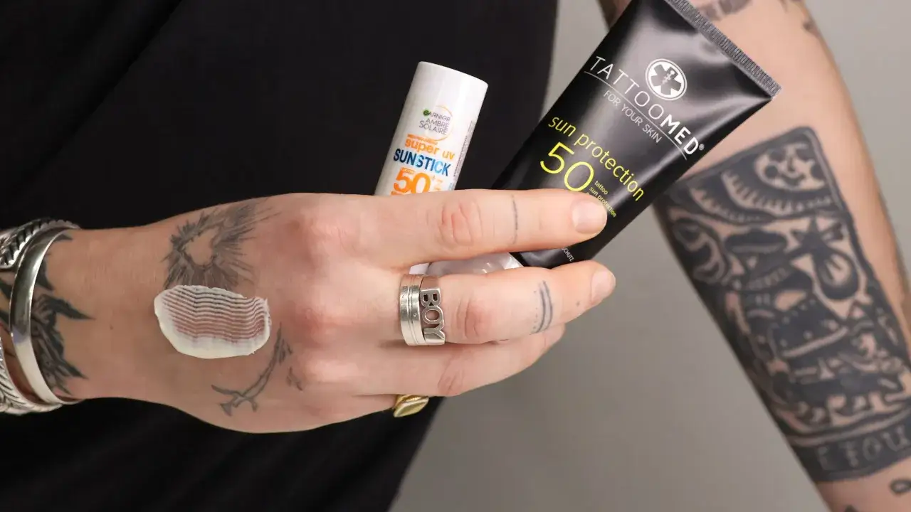 Hände mit Tattoos halten Sonnencreme. Die Frage