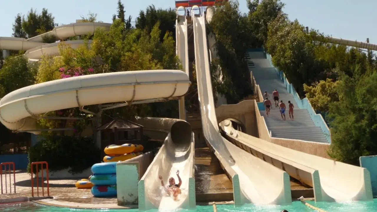 Zjeżdżalnie wodne na sandy beach faliraki by Sun Palace. Ludzie wchodzą po schodach, inni zjeżdżają.
