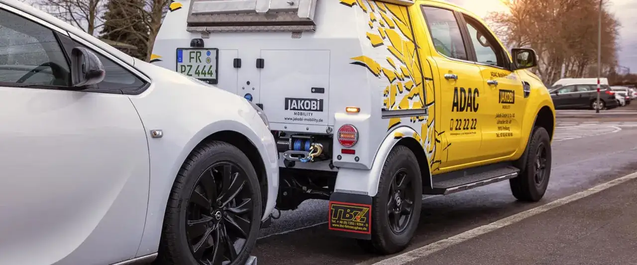 Ein gelber ADAC-Abschleppwagen mit JAKOBI MOBILITY-Aufschrift bereitet sich auf das Abschleppen eines wei&szlig;en PKW vor. Was ist beim Abschleppen zu beachten, PKW defekt?