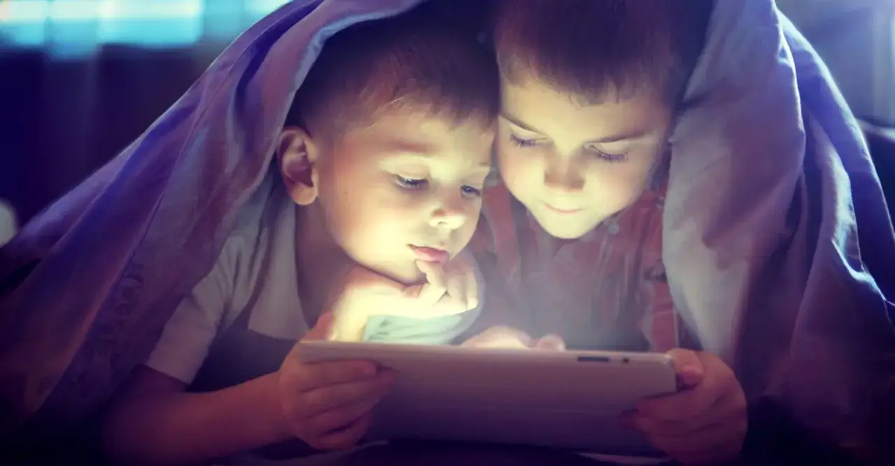 Dwóch chłopców pod kołdrą ogląda bajki edukacyjne dla 4 latka na tablecie.