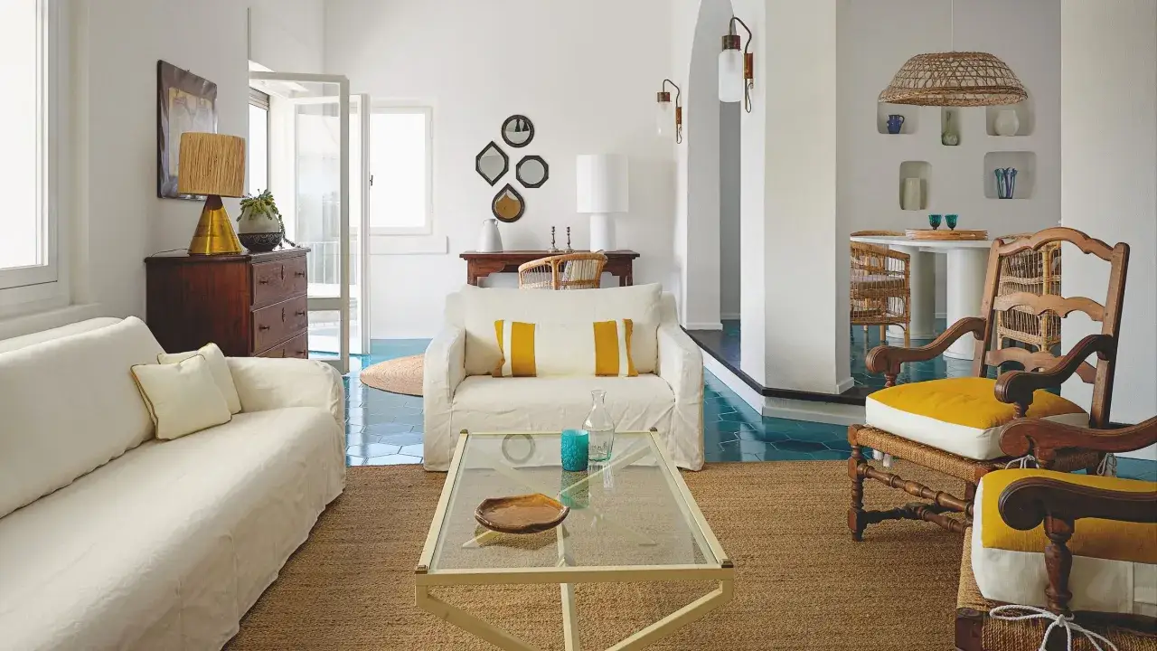 Arredamento B&B: divani bianchi, sedie in legno e vimini, tavolino in vetro, tappeto in juta e dettagli color ocra.