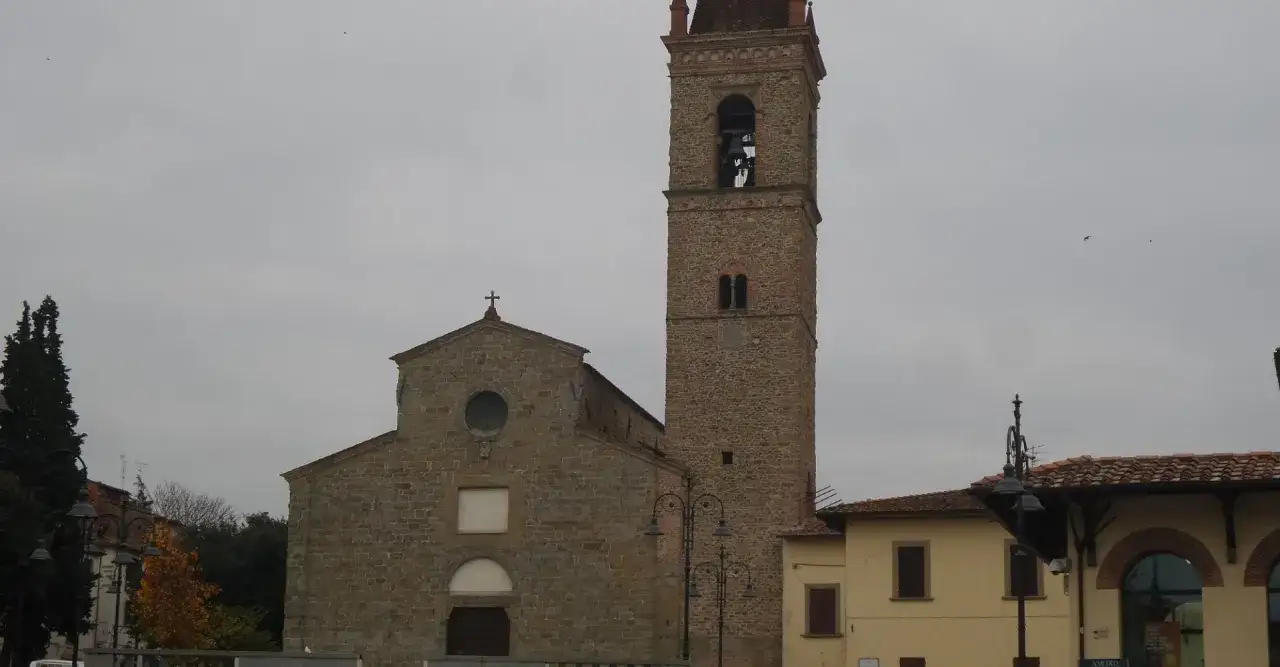 Un campanile in pietra domina la piazza, parte di un affascinante arezzo tour. Edifici storici e un cielo nuvoloso completano la scena.
