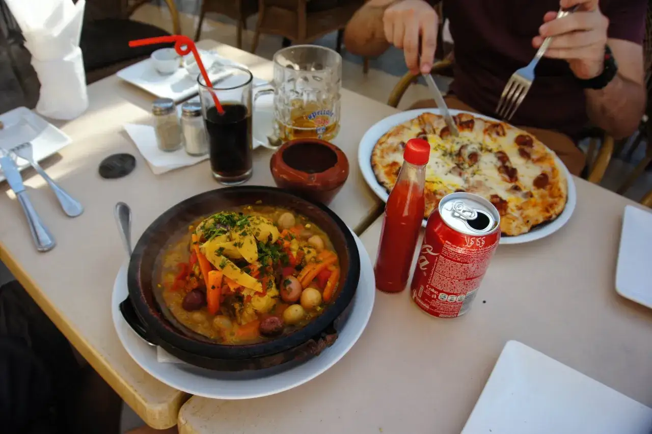 Kolacja w Maroku: aromatyczny tadżin, pizza i napoje. W tle piwo i cola, idealne do posiłku.