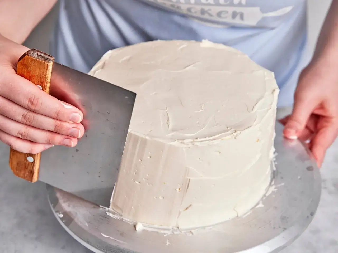 Eine Hand gl&auml;ttet mit einem Spachtel die italienische Buttercreme auf einem runden Kuchen.