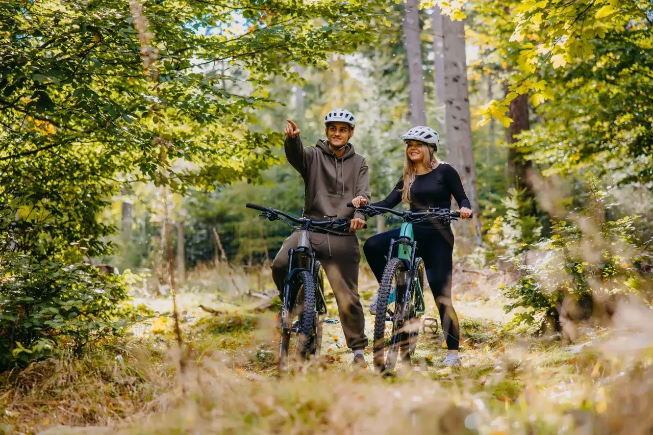Para na rowerach w lesie, odkrywająca malownicze **trasy rowerowe Szklarska Poręba**.