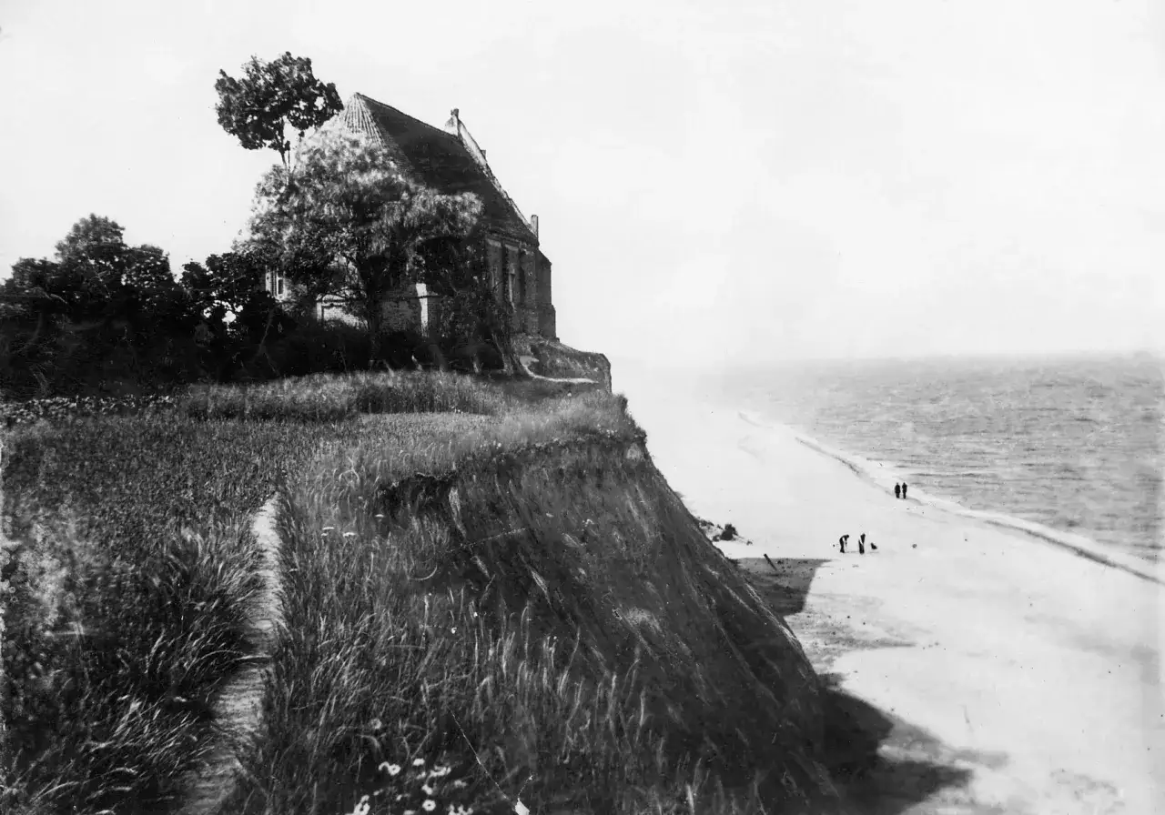 Dawny kościół na klifie nad morzem. Na plaży w Trzęsaczu widać kilka osób spacerujących.