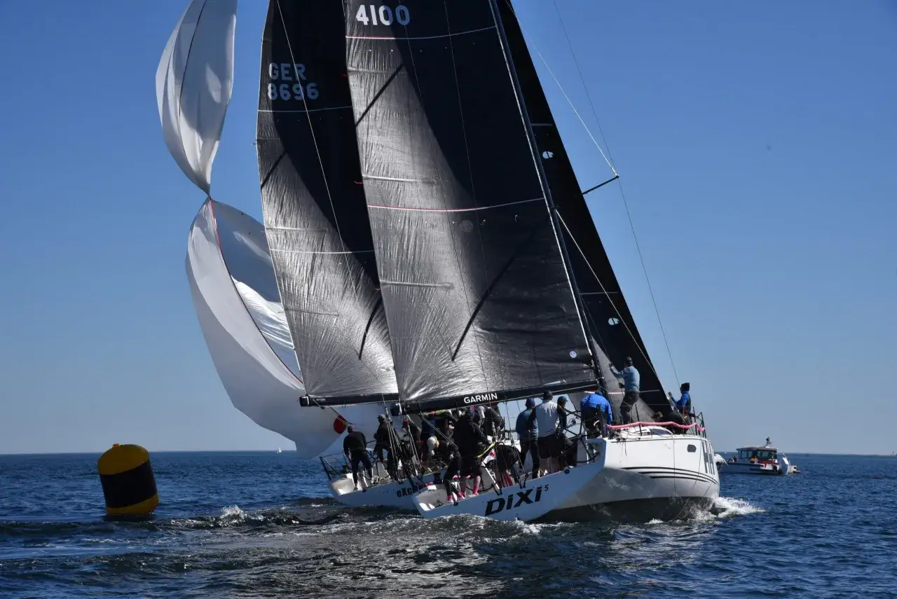 Segelregatta aktuell: Ein Segelboot mit schwarzen und wei&szlig;en Segeln k&auml;mpft sich durch die Wellen. Die Crew ist aktiv, um die Segel optimal einzustellen.