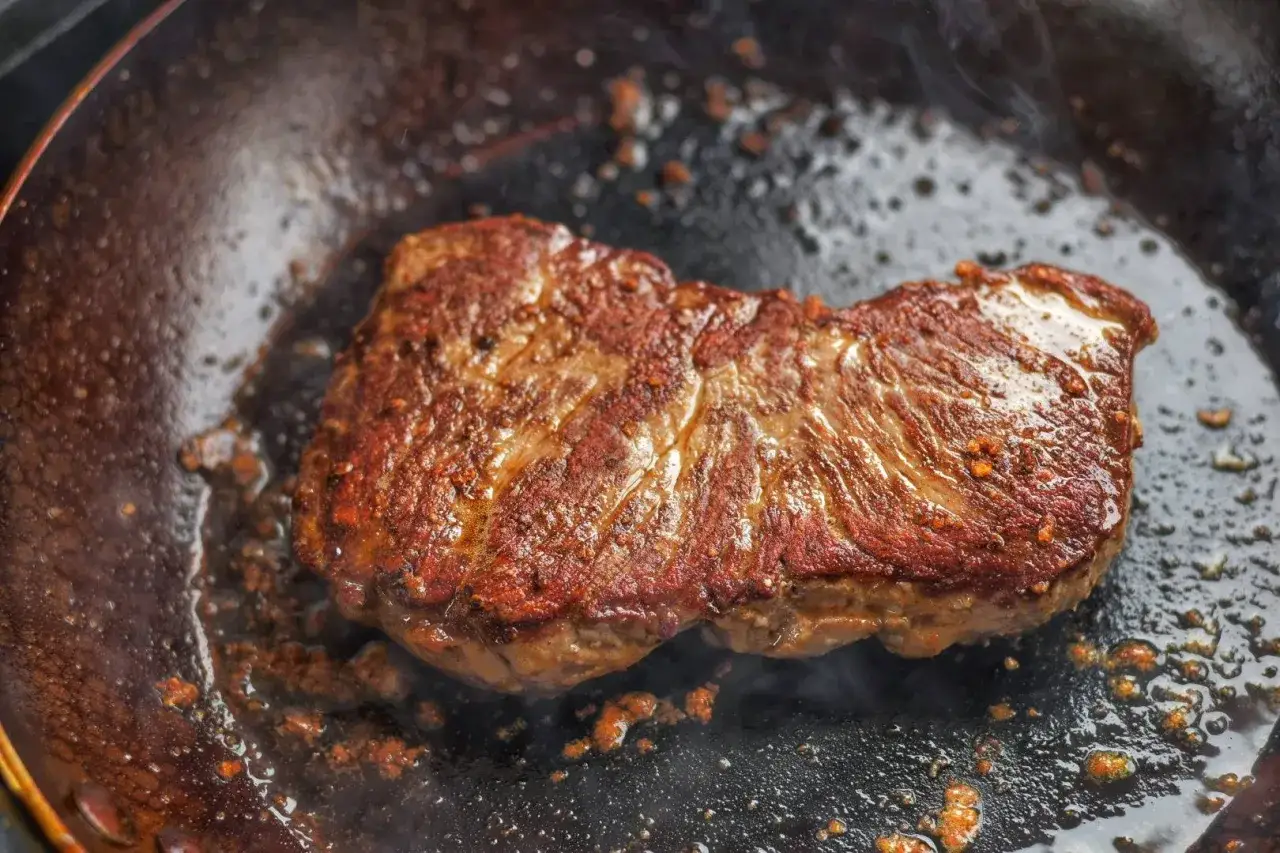 Ein saftiger Rumpsteak braten in einer hei&szlig;en Pfanne, Dampf steigt auf.