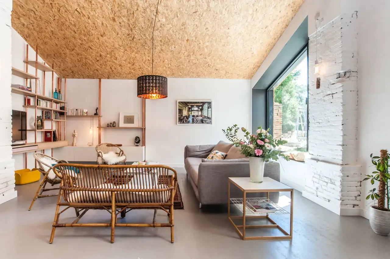 Salon moderne avec plafond en OSB sans formaldéhyde, mobilier en rotin et canapé gris.