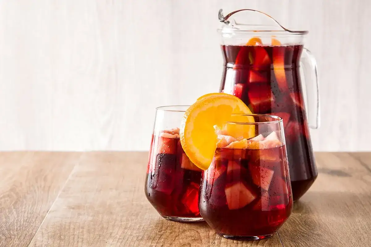 Orzeźwiająca sangria drink w dzbanku i dwóch szklankach, ozdobiona plasterkami pomarańczy i kawałkami owoców.