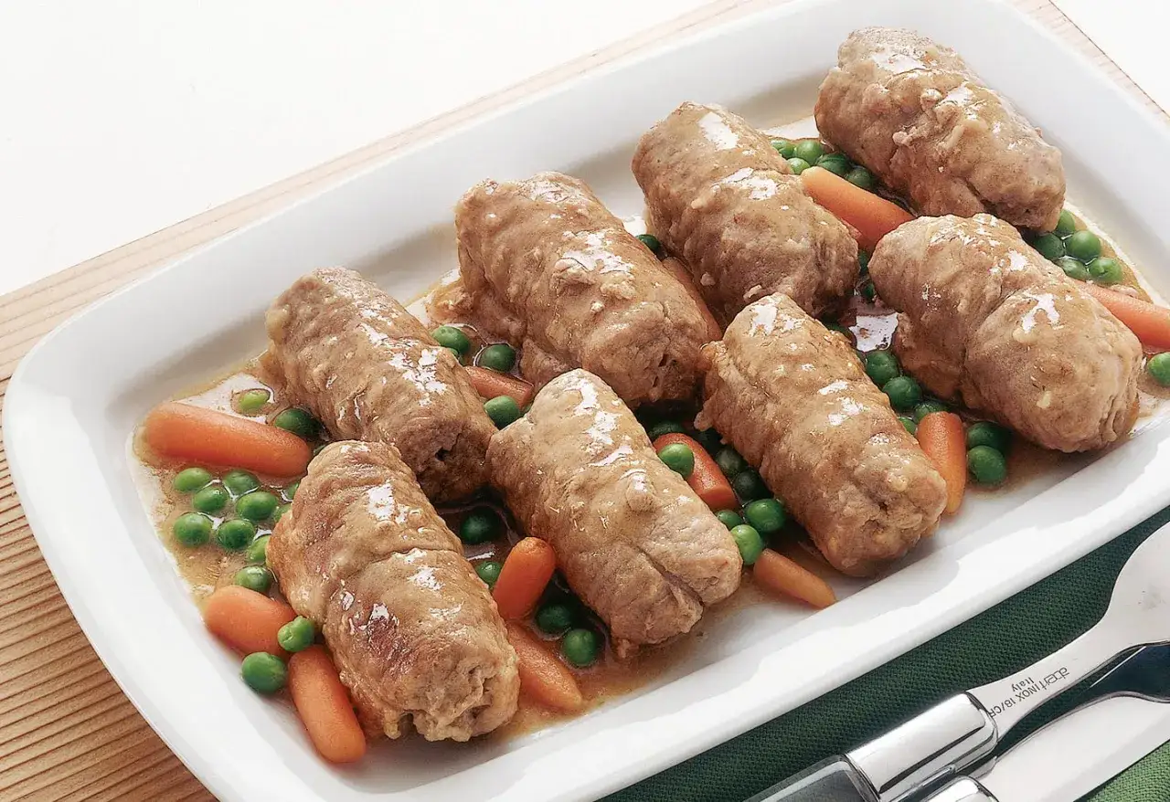 Involtini di carne succulenti in un piatto bianco con piselli e carote.