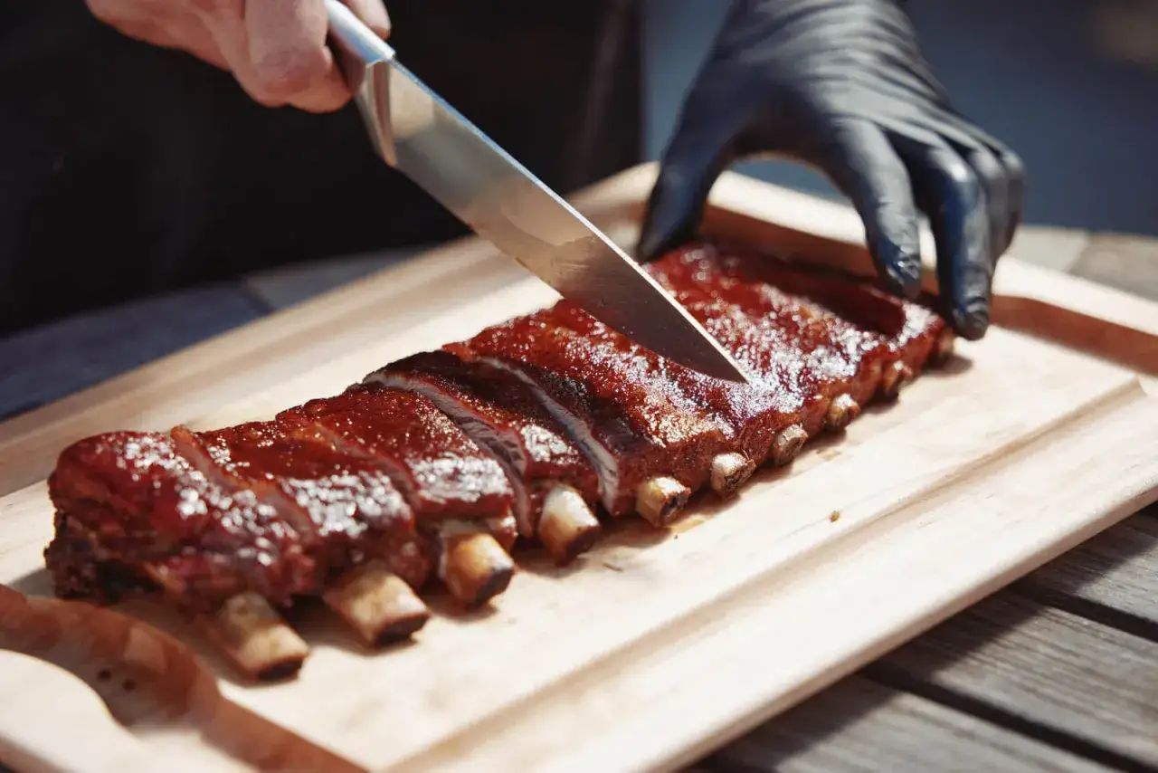 Fertig marinierte Spareribs werden auf einem Holzbrett angeschnitten. Perfekt f&uuml;r den Gasgrill!