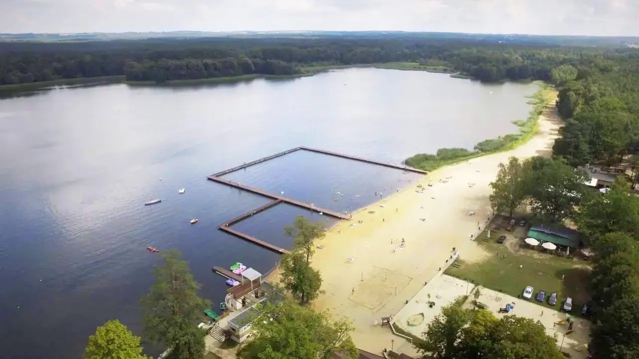 Wakacje nad jeziorem w Antoninie: piaszczysta plaża, drewniane pomosty i kąpielisko.