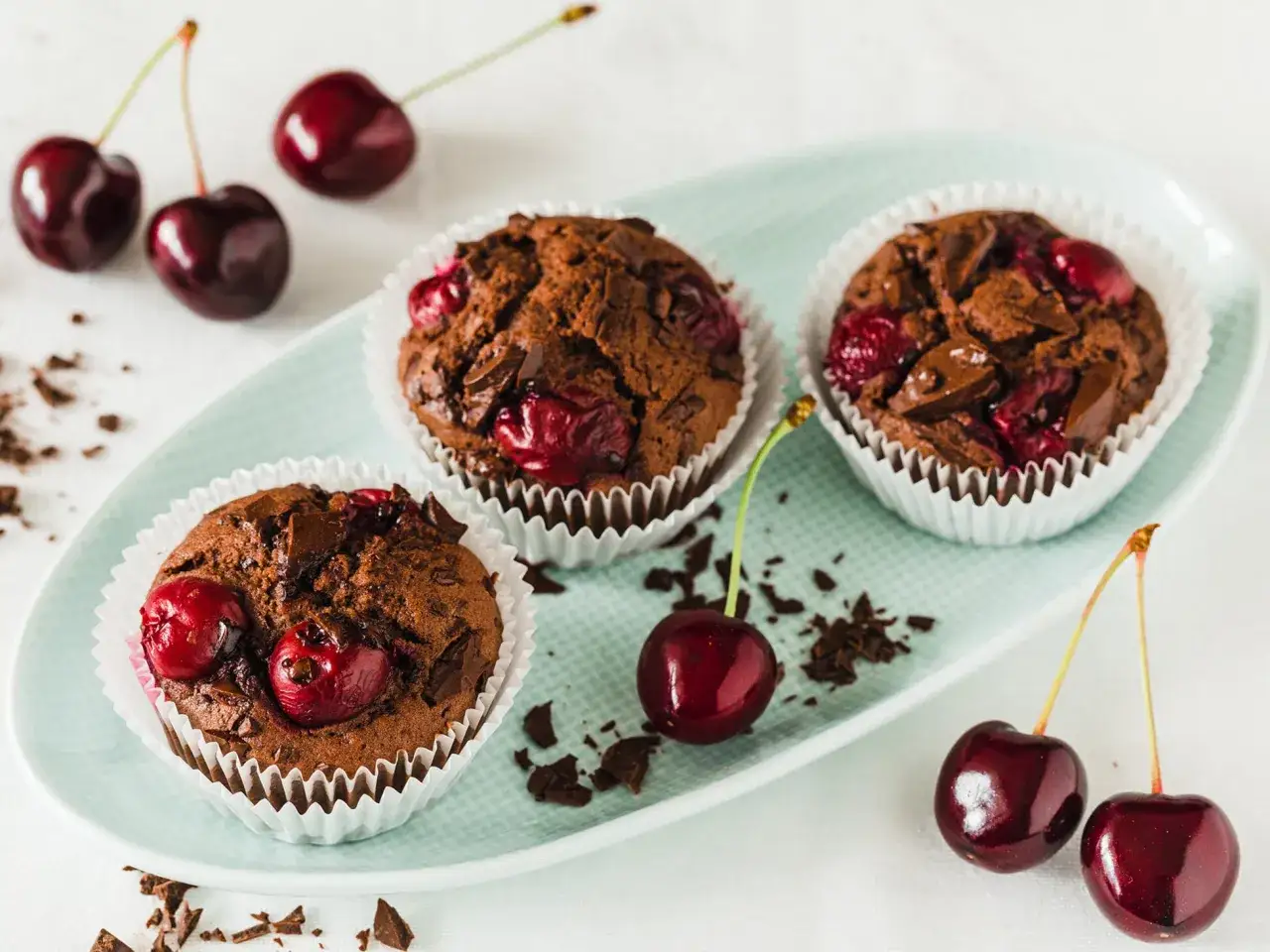 Schoko Kirsch Muffins mit frischen Kirschen und Schokostückchen auf einem hellblauen Teller.