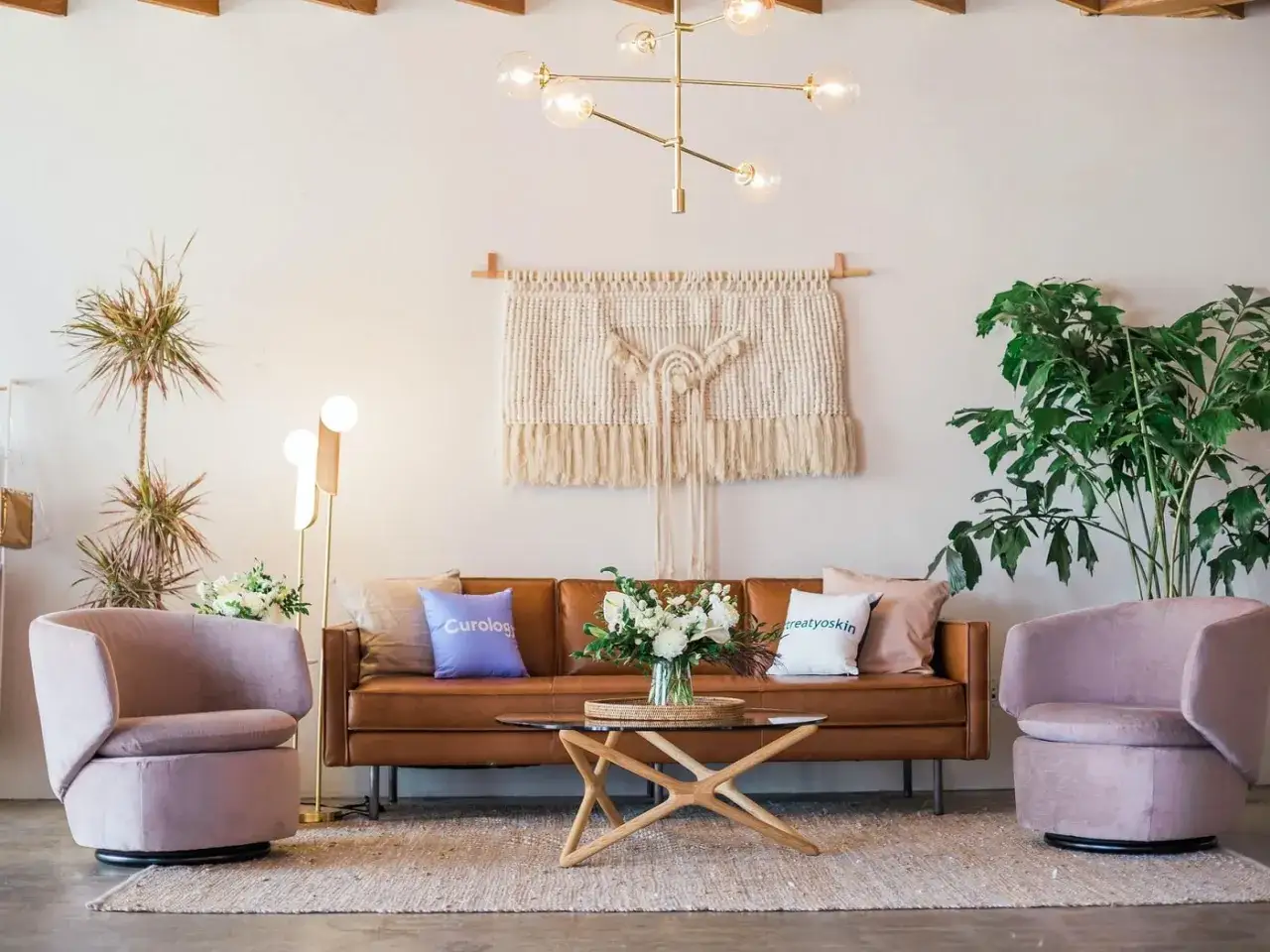 Salon moderne avec canapé en cuir marron, fauteuils roses poudrés, tapis en jute et macramé mural. La couleur peinture salon est neutre, mettant en valeur les meubles.