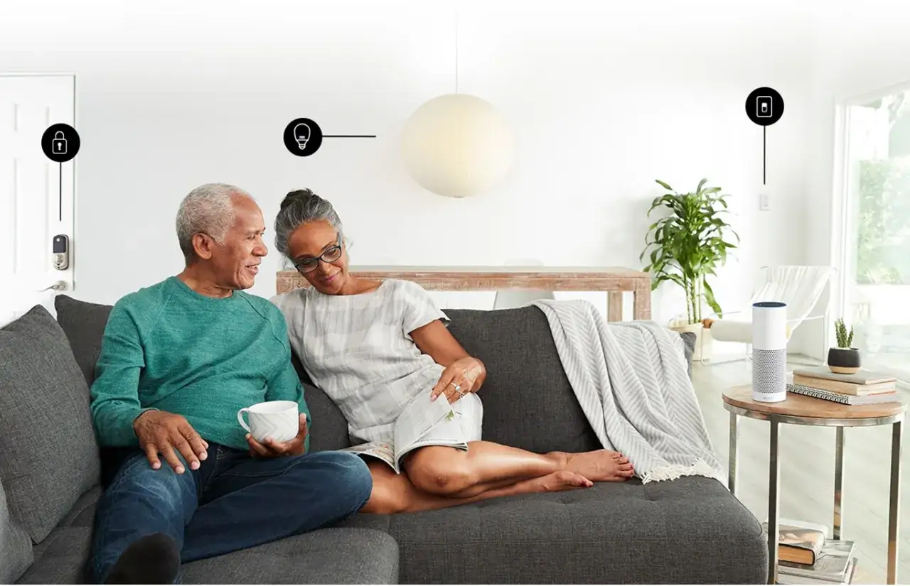 Un couple se détend sur un canapé, testant Alexa pour contrôler les lumières et la serrure de la porte.