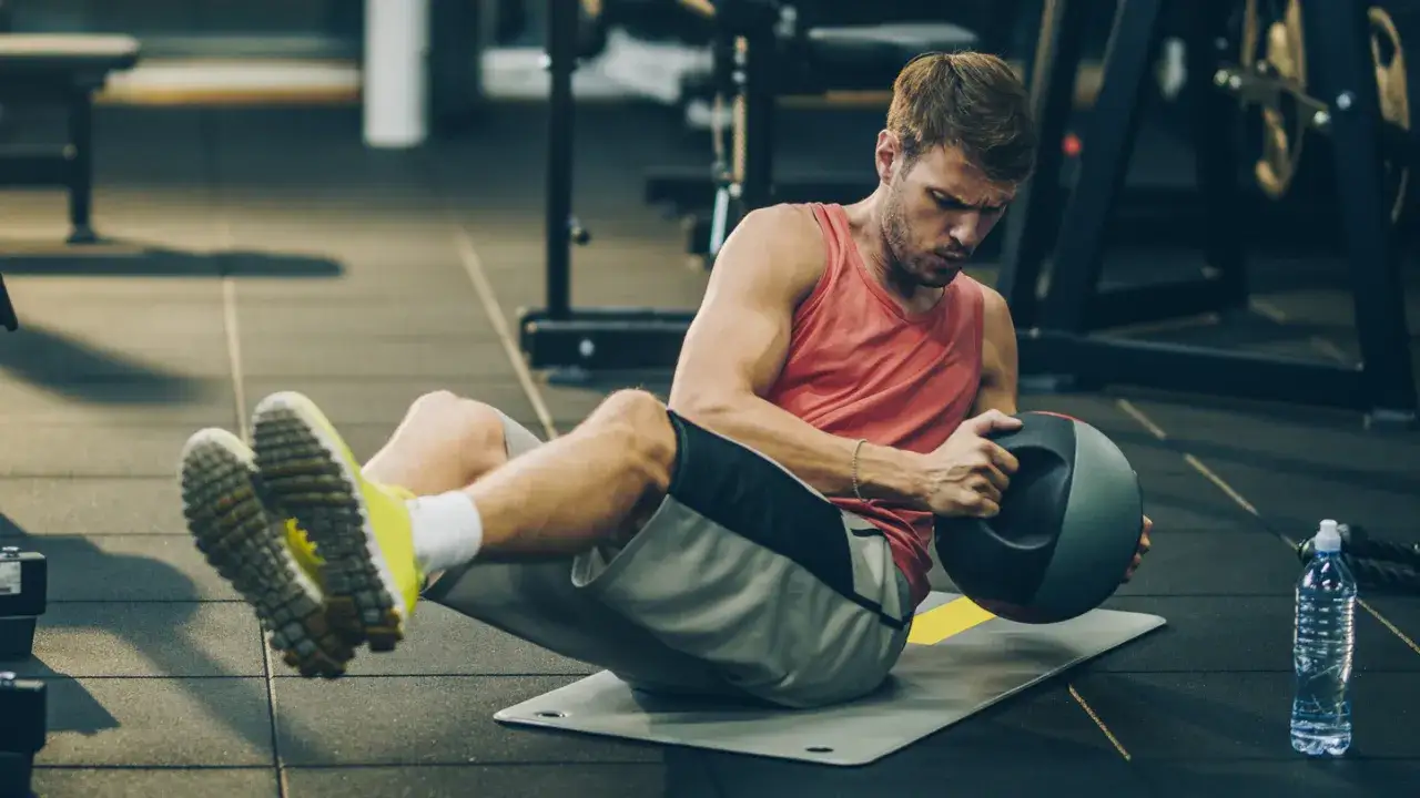 Uomo in palestra esegue un russian twist con palla medica, concentrato sull'allenamento addominale.