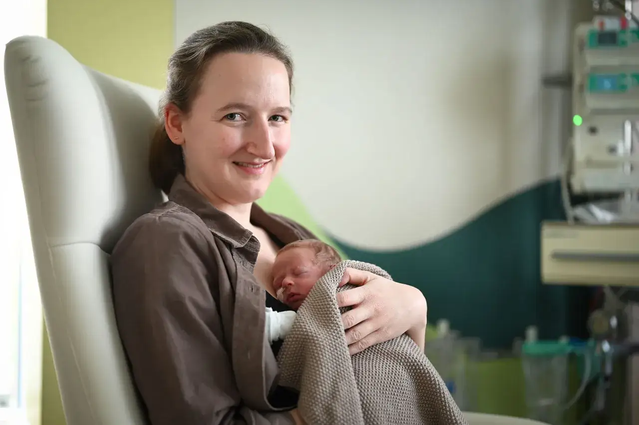 Gl&uuml;ckliche Mutter h&auml;lt ihr Neugeborenes im Arm. Die Frage, wie lange nach Geburt im Krankenhaus, ist hier nicht relevant, da die Szene Geborgenheit zeigt.