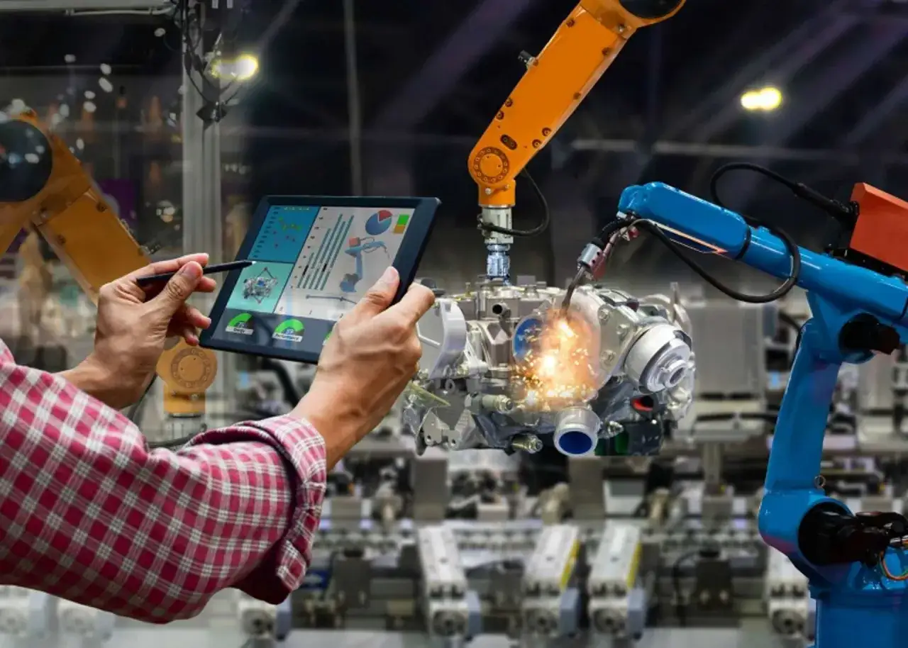 Un op&eacute;rateur supervise un **master genie m&eacute;canique** sur une tablette, tandis que des bras robotiques assemblent un moteur.