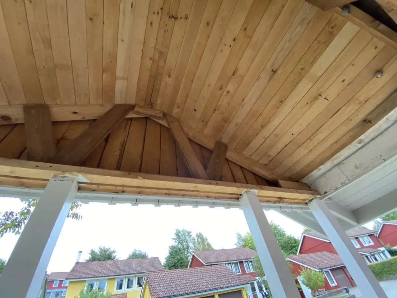 Taket på en farstukvist håller på att byggas. Träpanel och synliga bjälkar syns. Hus i bakgrunden.