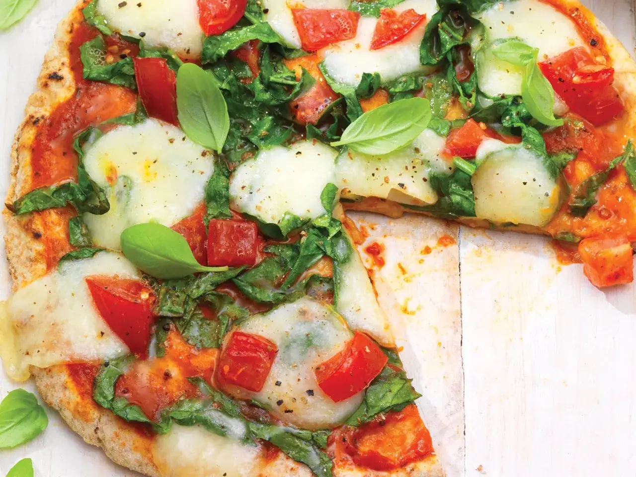 Eine köstliche Spinat Pizza mit frischen Tomaten und Mozzarella, garniert mit Basilikum.