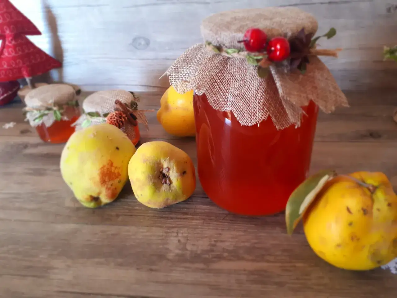 Barattolo di gelatina di mele cotogne, decorato con bacche rosse e spighe, circondato da mele cotogne fresche.