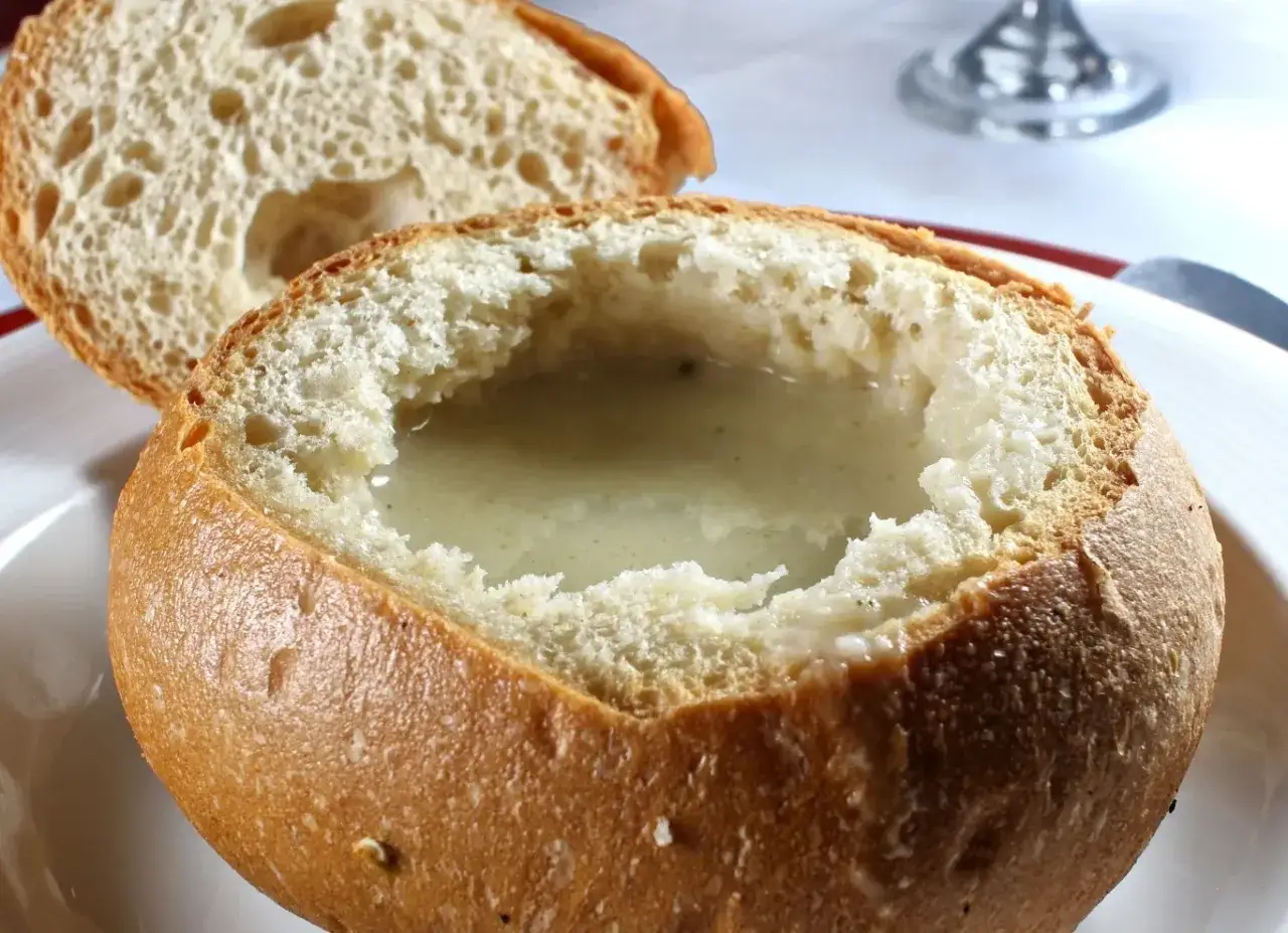 Chleb do żurku, wydrążony i wypełniony kremowym daniem, obok kromki świeżego pieczywa.