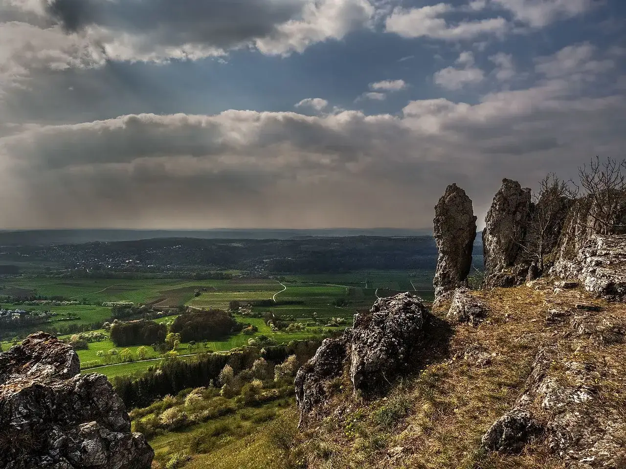 Felsformationen am Walberla, Blick über grüne Täler und Felder unter dramatischem Himmel. Ein toller Ort zum Walberla wandern.