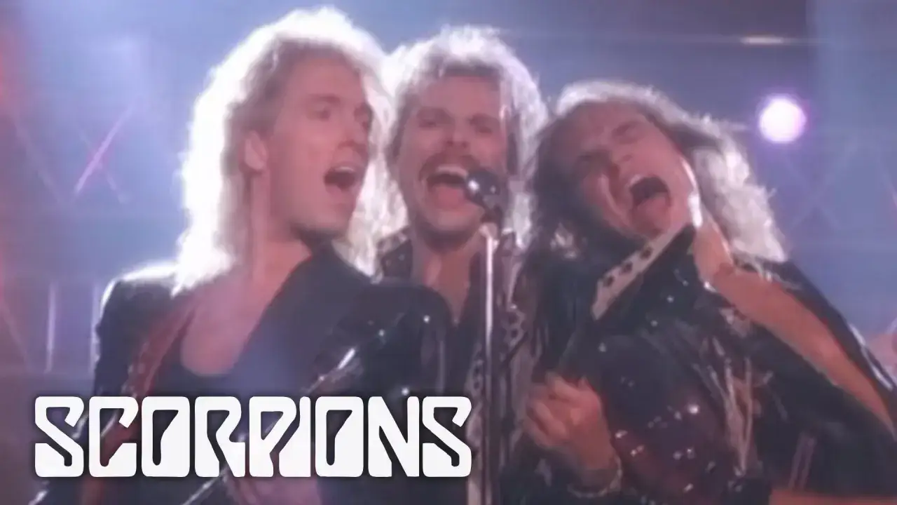 Scorpions śpiewają piosenki o miłości na koncercie. Wokalista z wąsem krzyczy do mikrofonu, otoczony przez kolegów z zespołu.