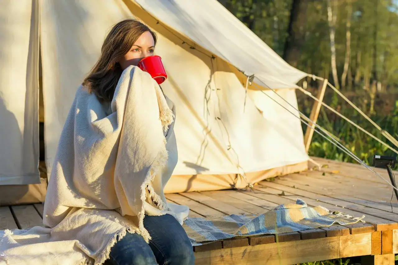 Kvinna med filt och röd mugg vid tältet. En mysig stund som visar vikten av en bra packlista camping.