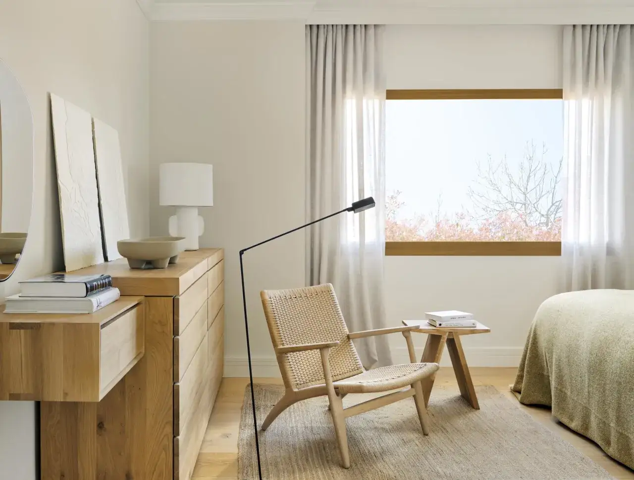 Habitación con decoración nórdica: cómoda de madera, sillón de mimbre y lámpara de pie.
