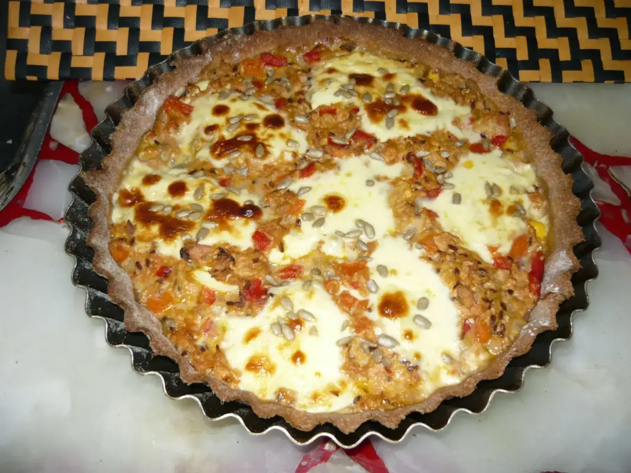 Tarta de atún recién horneada, con queso fundido, pimientos rojos y semillas de girasol. ¡Un manjar!