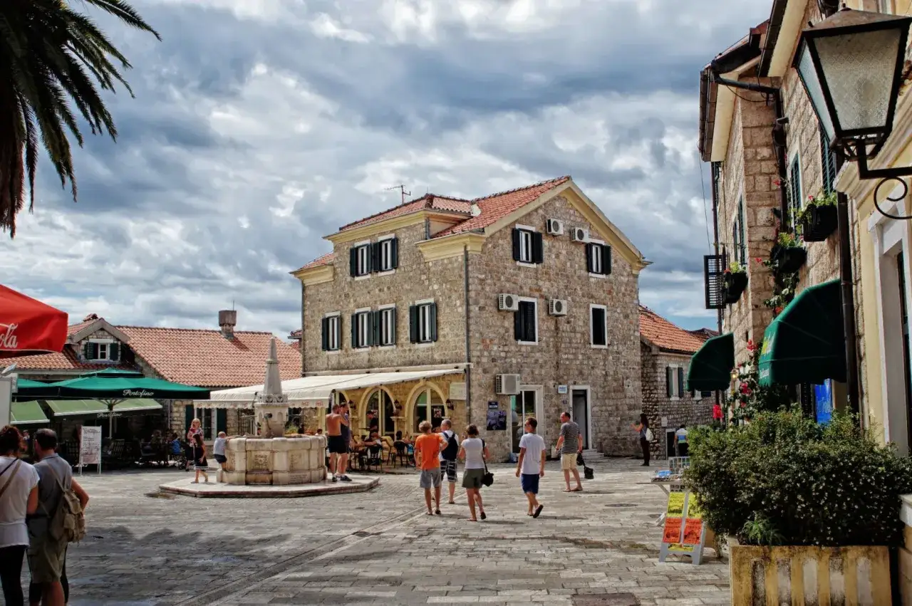 Spacerem po urokliwym placu w Herceg Novi, Czarnogóra, z kamiennymi budynkami i fontanną.