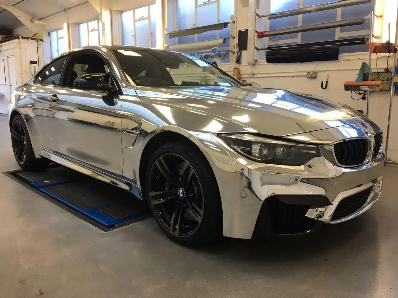 Lśniący, chromowany samochód BMW M4 w warsztacie. Jego lustrzana powierzchnia odbija światło i otoczenie.