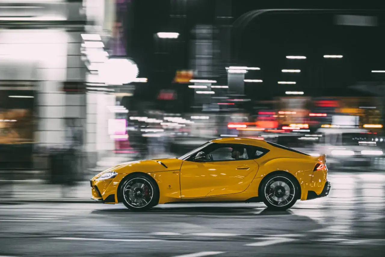 Żółta Toyota Supra pędzi nocą przez miasto, a jej moc (toyota supra ile ma koni) jest odczuwalna w rozmazanych światłach.
