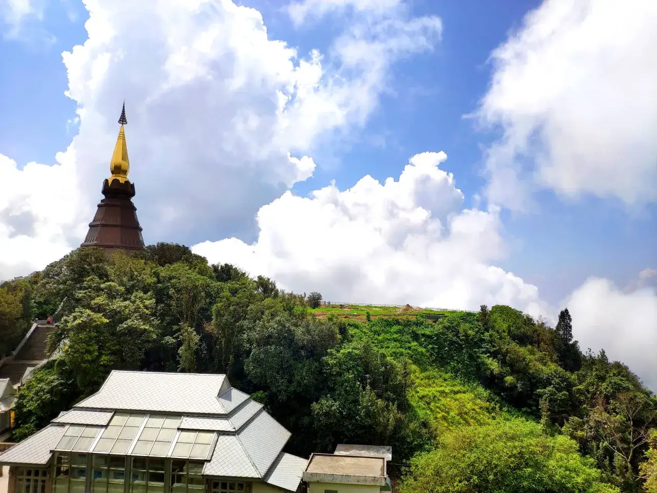 Złota pagoda na szczycie Doi Inthanon, otoczona bujną zielenią i chmurami.