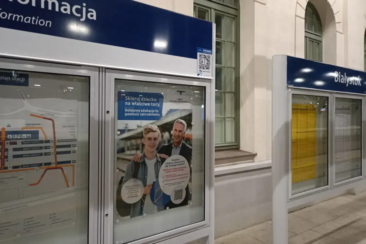 Na dworcu kolejowym w Białymstoku, obok mapy stacji, plakat zachęca do edukacji kolejowej. Skanując kod QR, dowiesz się, jak sprawdzić skąd jedzie pociąg.