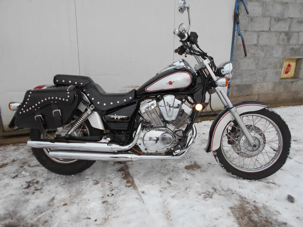 Czarny motocykl Zipp Roadstar 250 z sakwami, błyszczącymi chromami i ozdobnymi nitami, stoi na zaśnieżonym podjeździe.