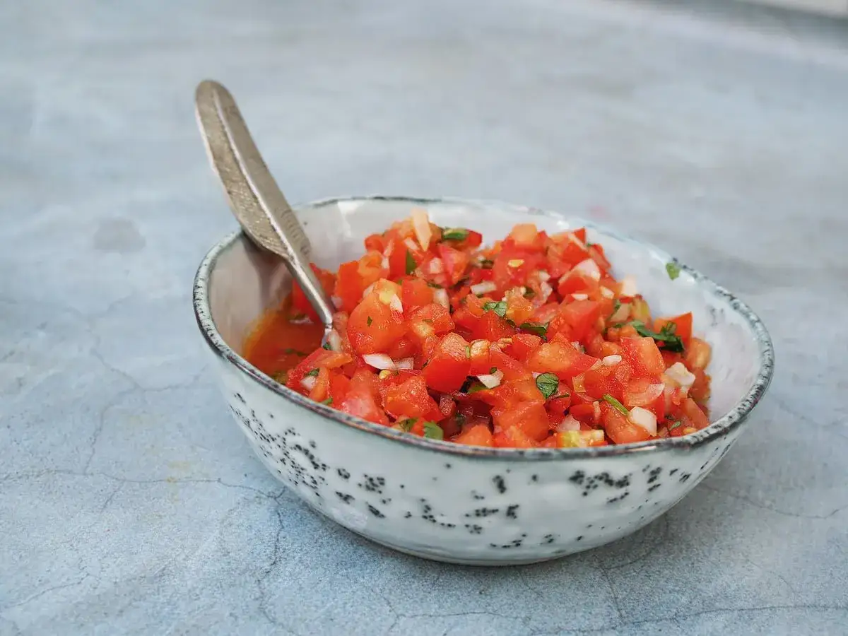 En sk&aring;l med f&auml;rsk pico de gallo, perfekt f&ouml;r ditt salsa recept. Tomater, l&ouml;k och &ouml;rter blandas i en rustik sk&aring;l med en dekorativ sked.