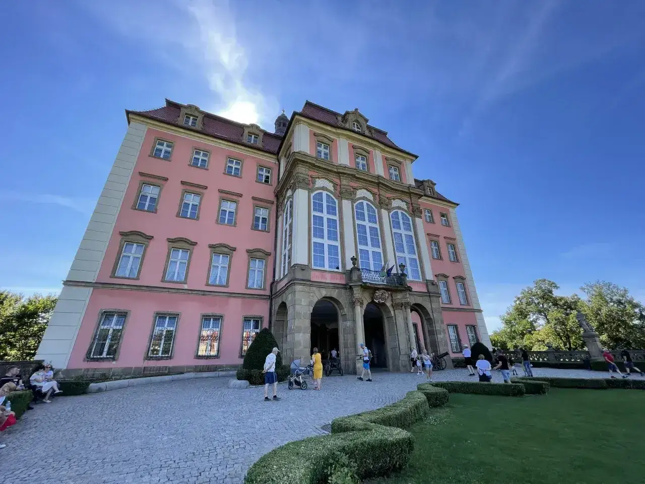 Zamek Książ, malowniczo położony, łatwy dojazd PKP. Turyści zwiedzają barokową budowlę w słoneczny dzień.