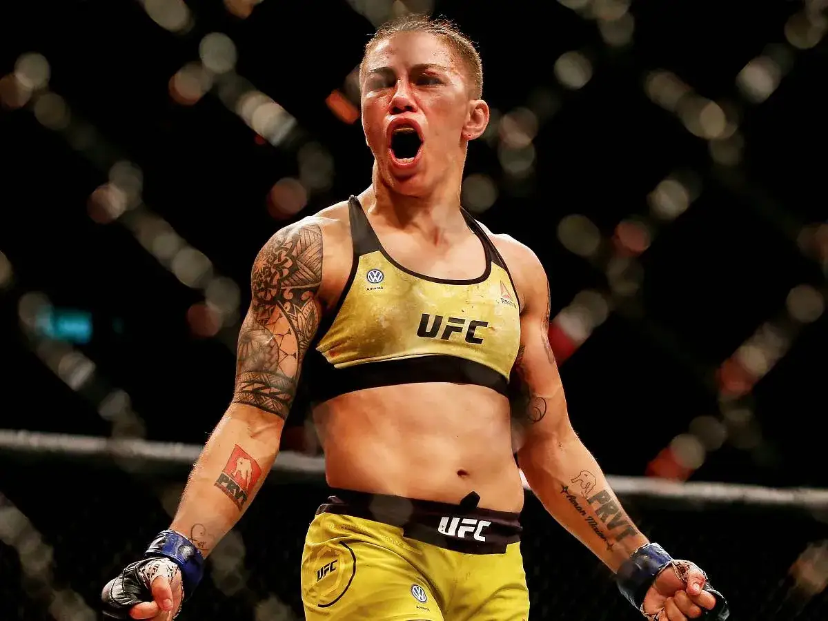 Jessica Andrade, en UFC-fighter, vr&aring;lar i seger i oktagonen. Hennes tatuerade armar och gula UFC-kl&auml;der visar hennes styrka.